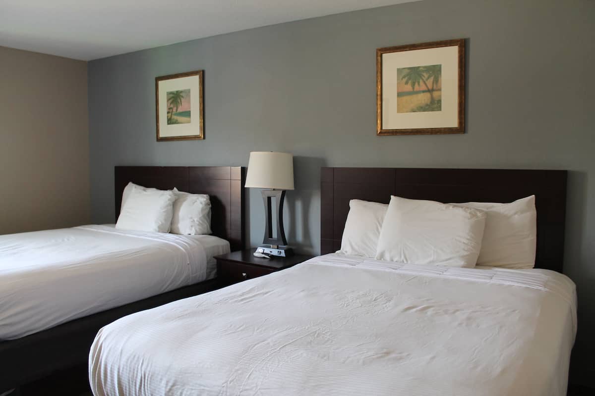 A hotel room with two beds, a nightstand with a lamp, and two framed pictures on the wall.