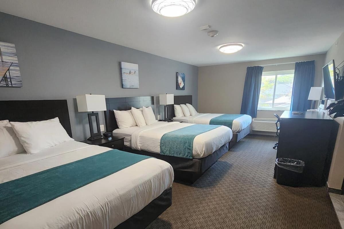 A hotel room with two beds, a desk, a chair, and a TV.
