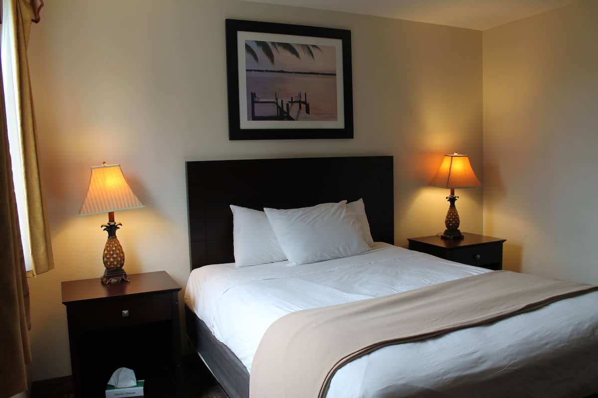 A hotel room with a bed, two bedside tables with lamps, a framed picture on the wall, and a window with curtains.