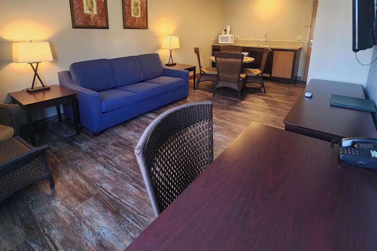 A living room with a blue sofa, two side tables with lamps, a dining area with a table and chairs, and a TV mounted on the wall.