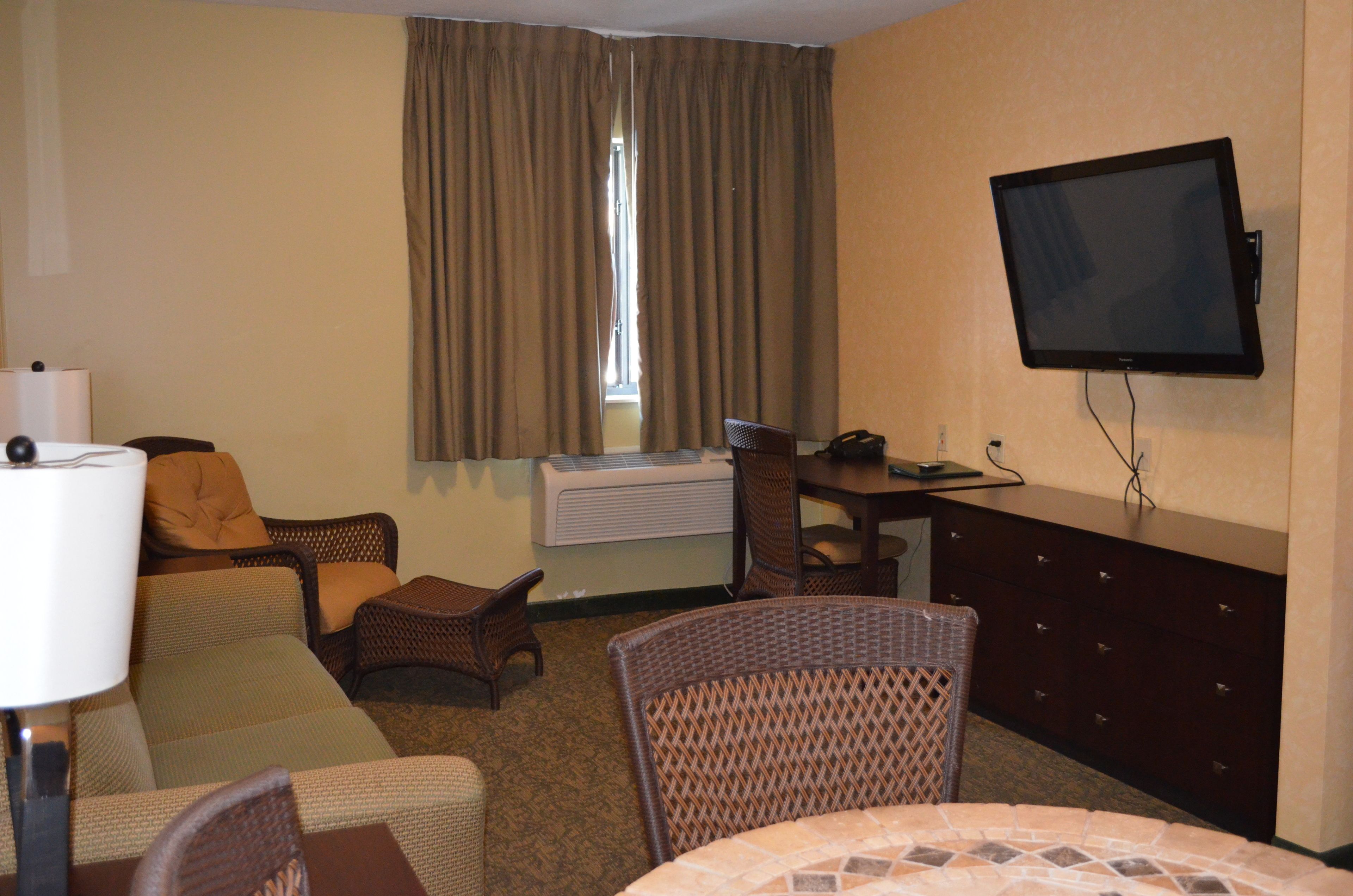 Een hotelkamer met een flatscreen televisie, een bureau, een stoel, een bank en een raam met gordijnen.