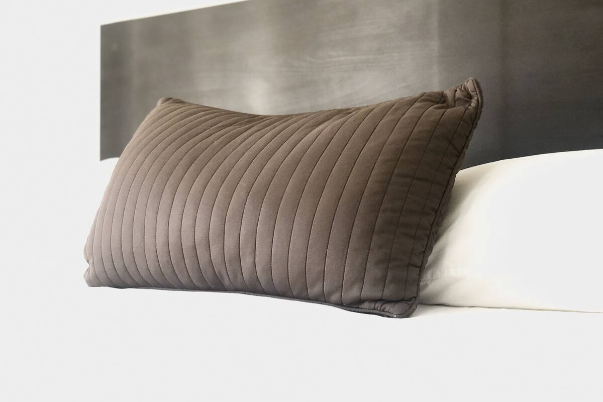 A pillow with a ribbed texture placed on a bed with a white pillow and a dark headboard.