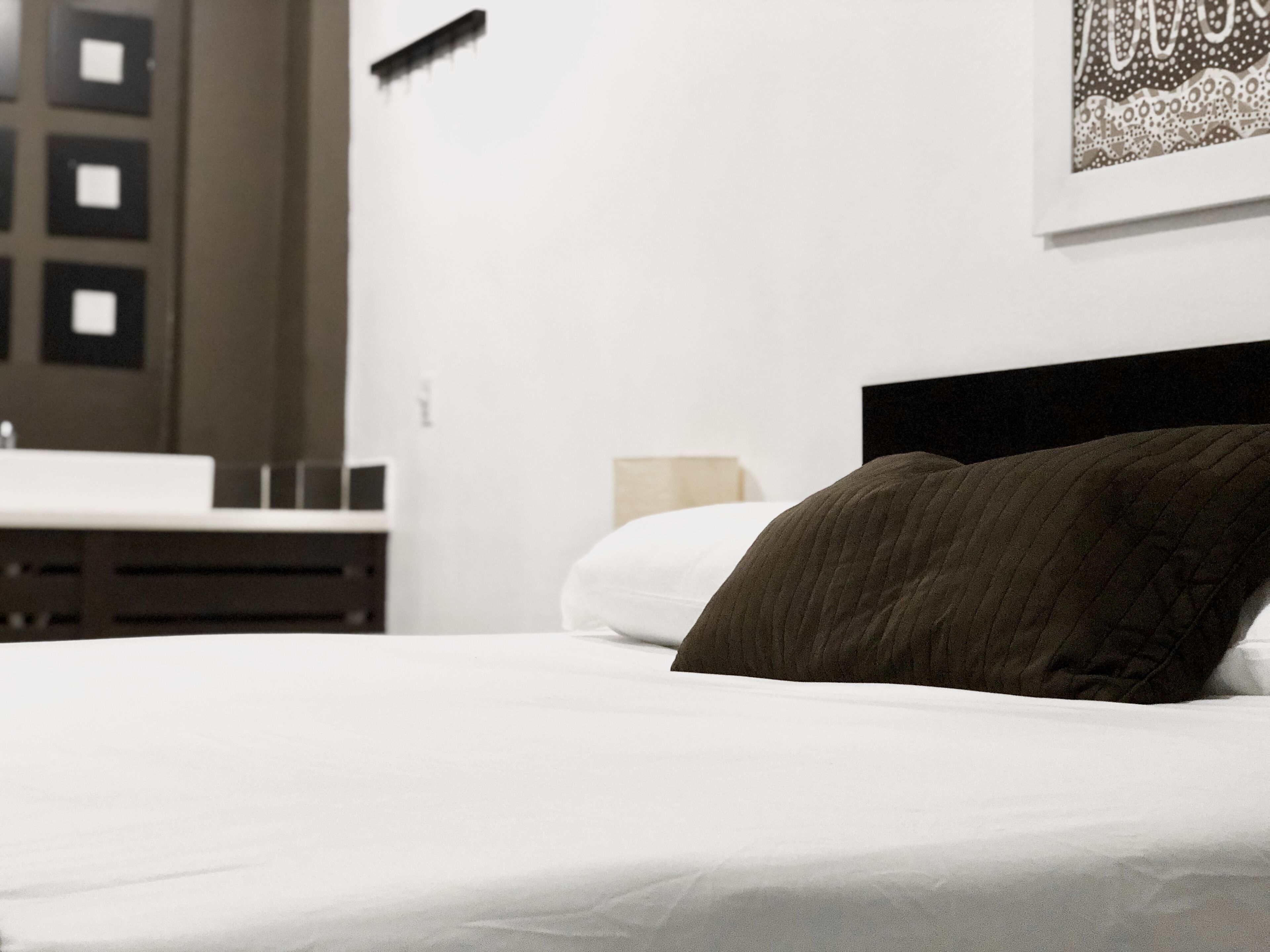 A neatly made bed with a dark headboard, a white pillow, and a white mattress cover.