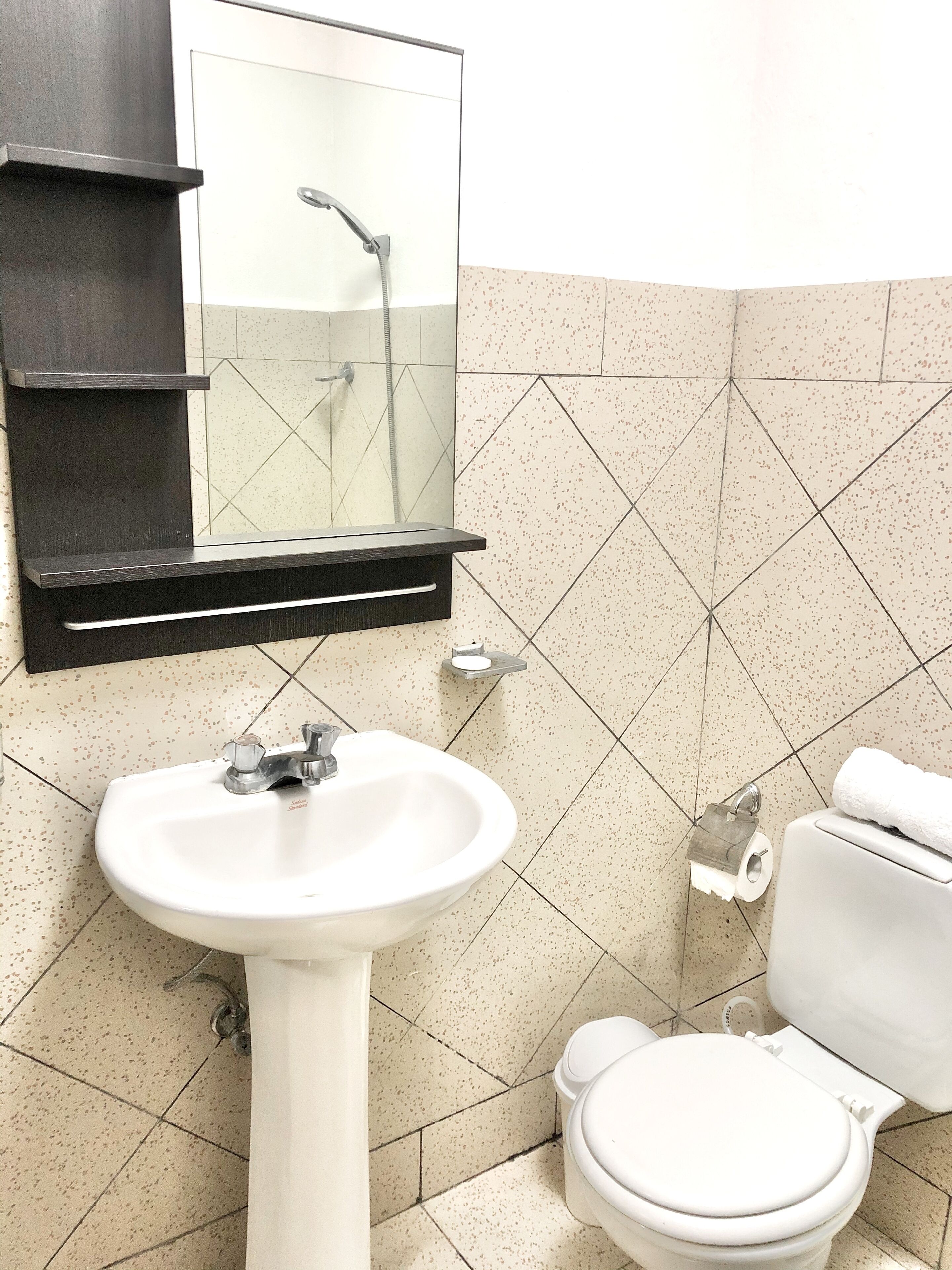 Un baño con lavamanos blanco, espejo, inodoro y ducha.