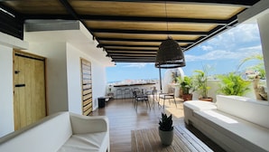 A covered outdoor seating area with a wooden ceiling, white sofas, and a wooden table. - Ocean Breeze (Santo Domingo)