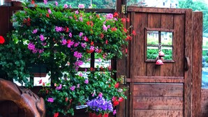 A wooden door with a small window, a wooden table with a red pot of flowers, and a wooden sculpture. - ALBERGO ALPENROSE Ski&Bike Mountain Hotel (Gressoney-Saint-Jean)