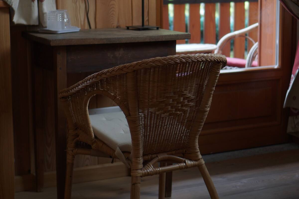 A wicker chair in a room with a wooden desk, a mirror, and a window with curtains.