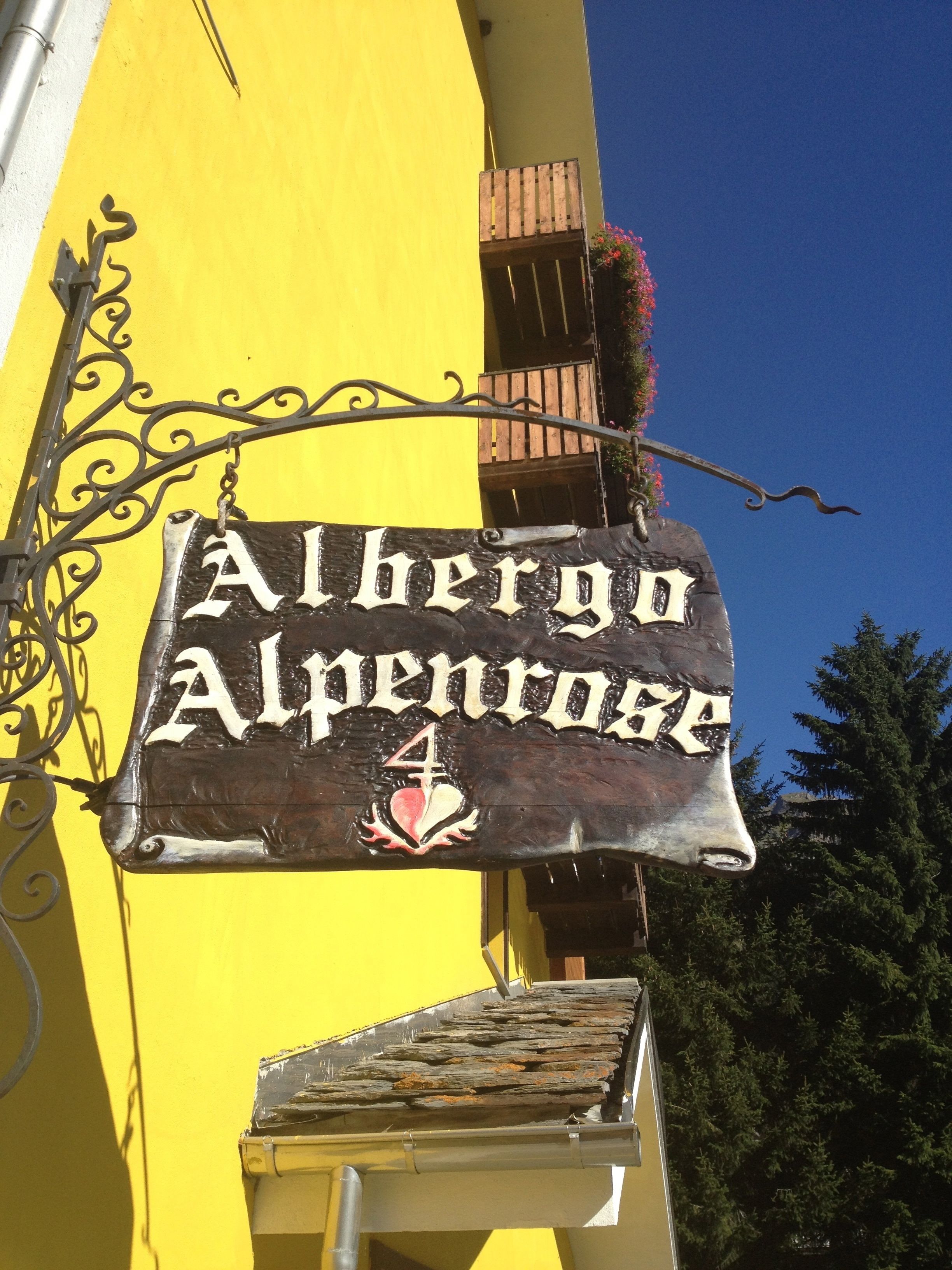 Une enseigne pour «Alhengo Alpenrose», au design rustique, fixée sur un bâtiment jaune doté d’un balcon en bois et d’une rambarde en métal.