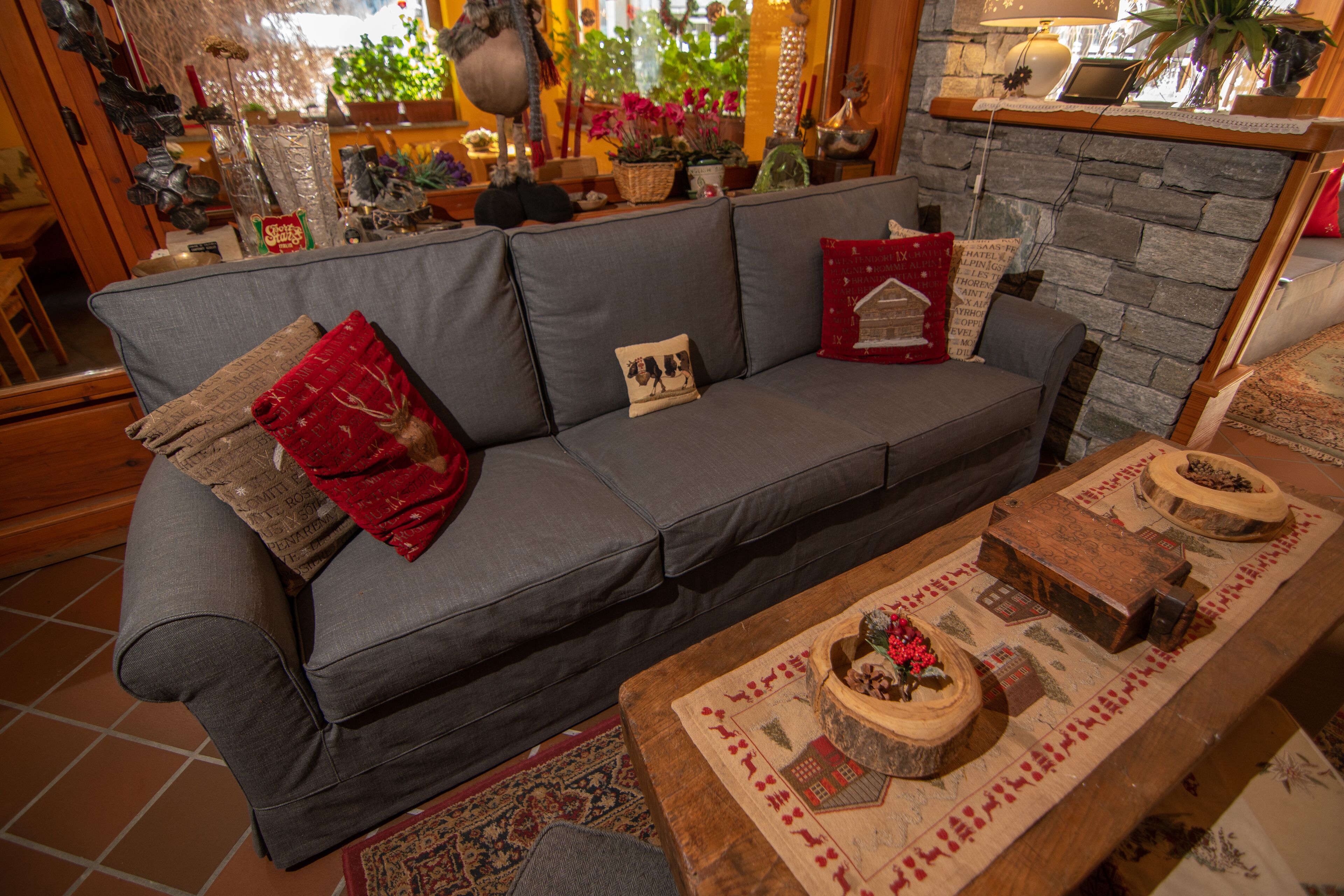 A cozy living room with a grey sofa, a wooden coffee table with decorative items, and a stone wall.