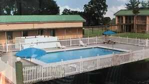 Une piscine entourée d’une clôture blanche, avec des chaises longues et des parasols.