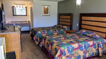 A room with two beds, a wooden dresser, a desk with a computer, and a mirror with lights.