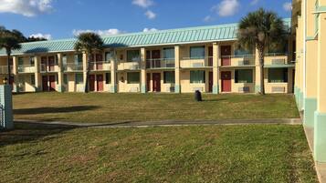 A motel with a green roof, multiple balconies, and a grassy courtyard.