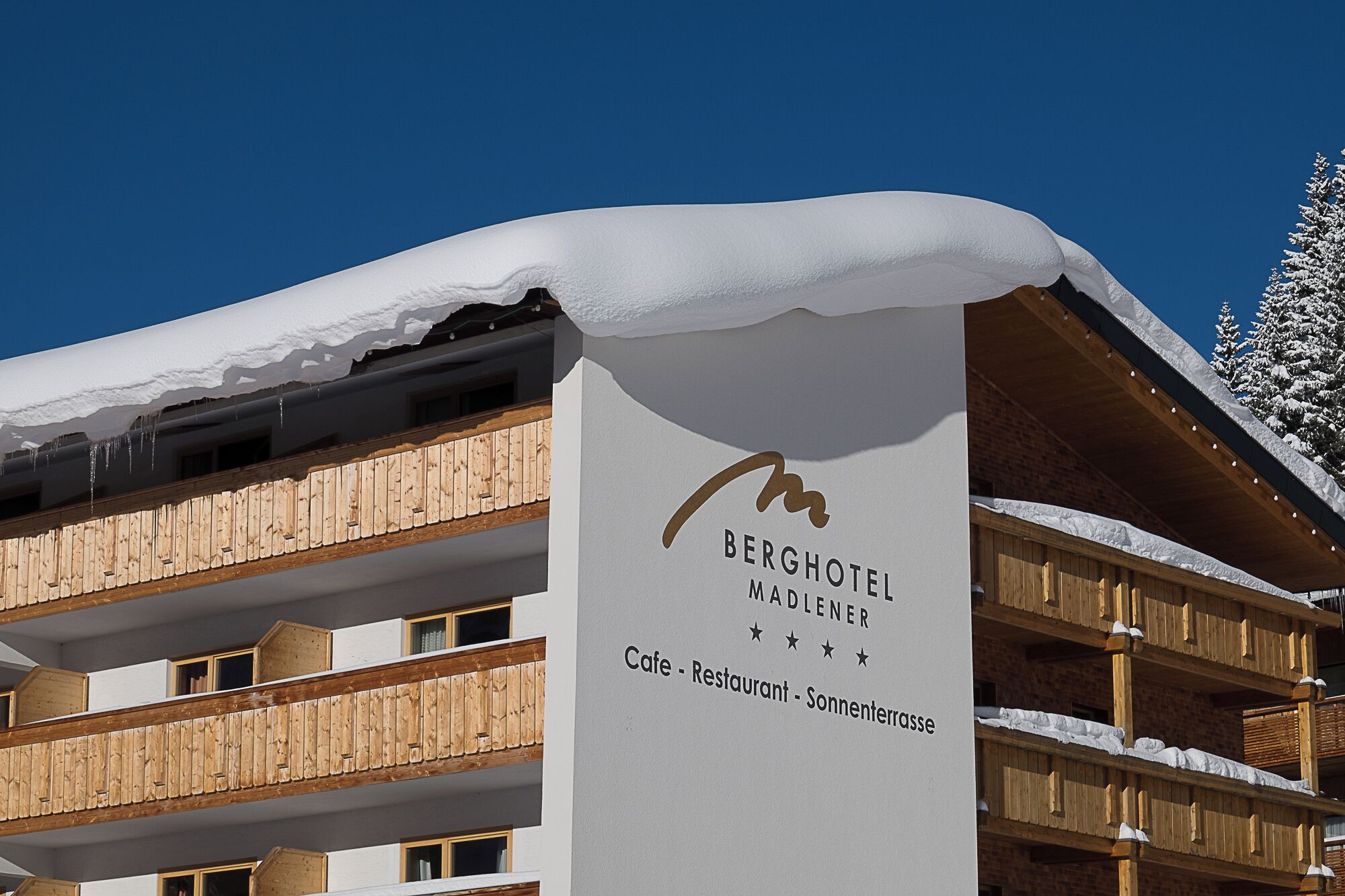 Ein Hotel Schild mit dem Namen 'BERGHOTEL MADLENER' und der Information, dass es ein Café, ein Restaurant und eine Sonnenterrasse gibt.