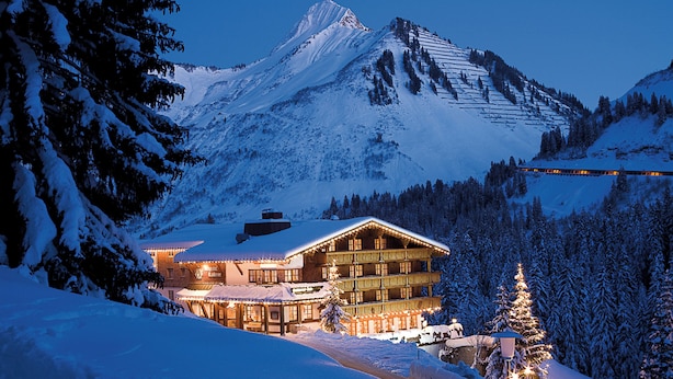 A snow-covered mountain with a ski resort building featuring multiple balconies and a lit Christmas tree.