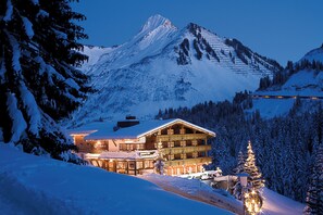 Een met sneeuw bedekte berg met een skigebouwbalkon met meerdere balkons en een verlichte kerstboom.