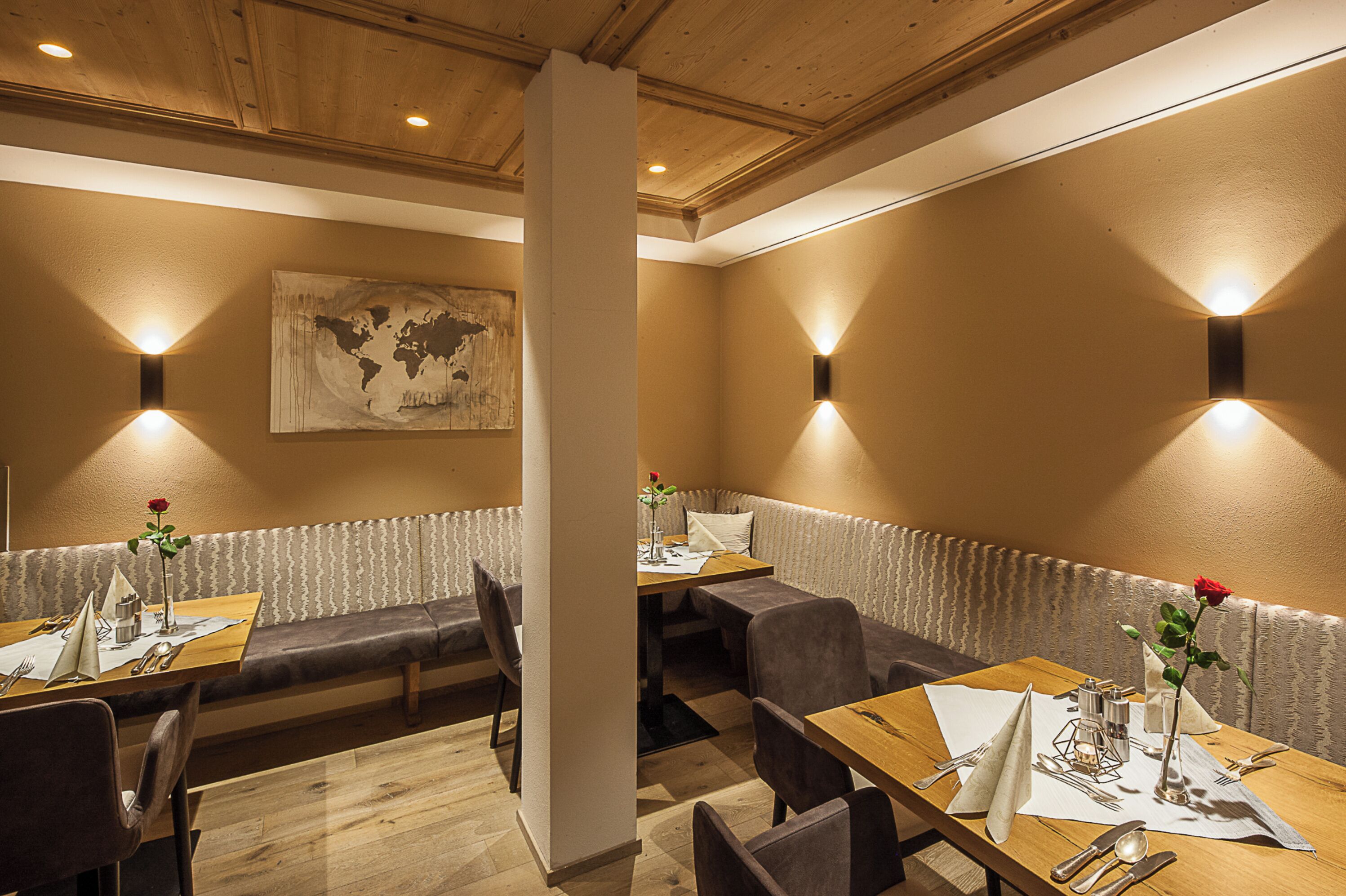 A restaurant with wooden tables and benches, a world map on the wall, and wall-mounted lighting.