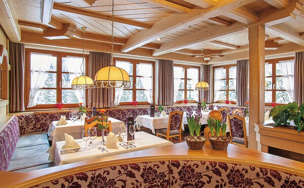 A dining area with wooden beams, large windows, and a central table set for dining.