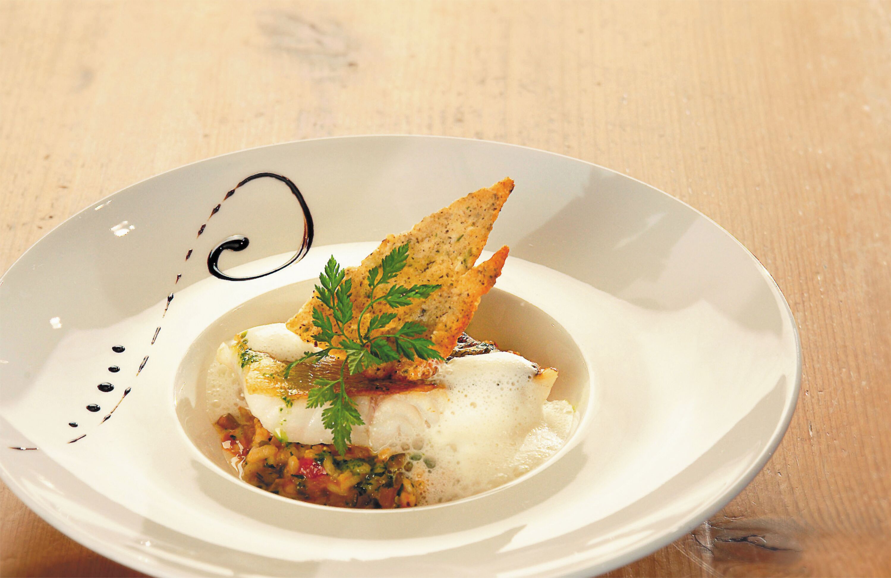 A white plate with a fish dish, garnished with parsley, and a piece of bread.