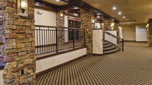 A hotel lobby with stone walls, a patterned carpet, and a staircase with a black railing. - The Lodge at Old Kinderhook Golf Resort (Camdenton)