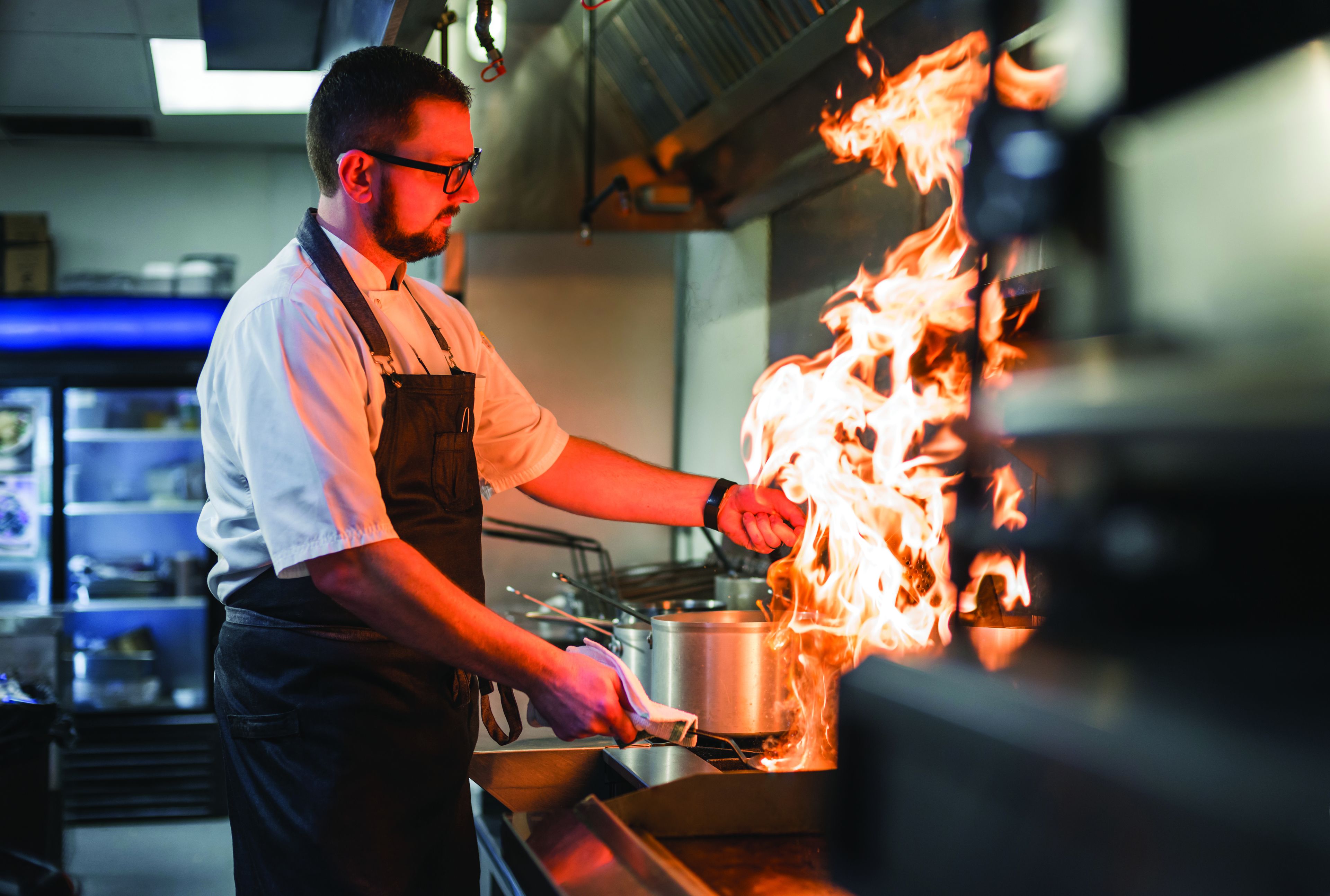 Un chef cocina a las llamas en una estufa en una cocina profesional.
