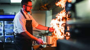 Un chef cocina a las llamas en una estufa en una cocina profesional.