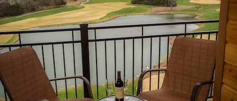 A balcony with two chairs and a table, overlooking a golf course and a lake.