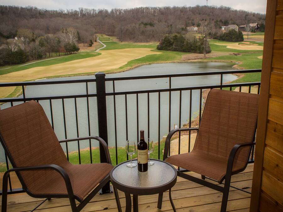A balcony with two chairs and a table, overlooking a golf course and a lake.