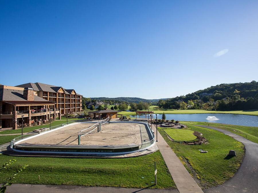 A golf course with a putting green, a clubhouse, and a lake in the background.