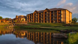 A multi-story hotel with balconies, a pond in front, and a golf course nearby. - The Lodge at Old Kinderhook Golf Resort (Camdenton)