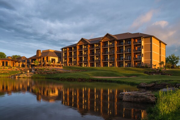 A multi-story hotel with balconies, a pond in front, and a golf course nearby. - The Lodge at Old Kinderhook Golf Resort (Camdenton)