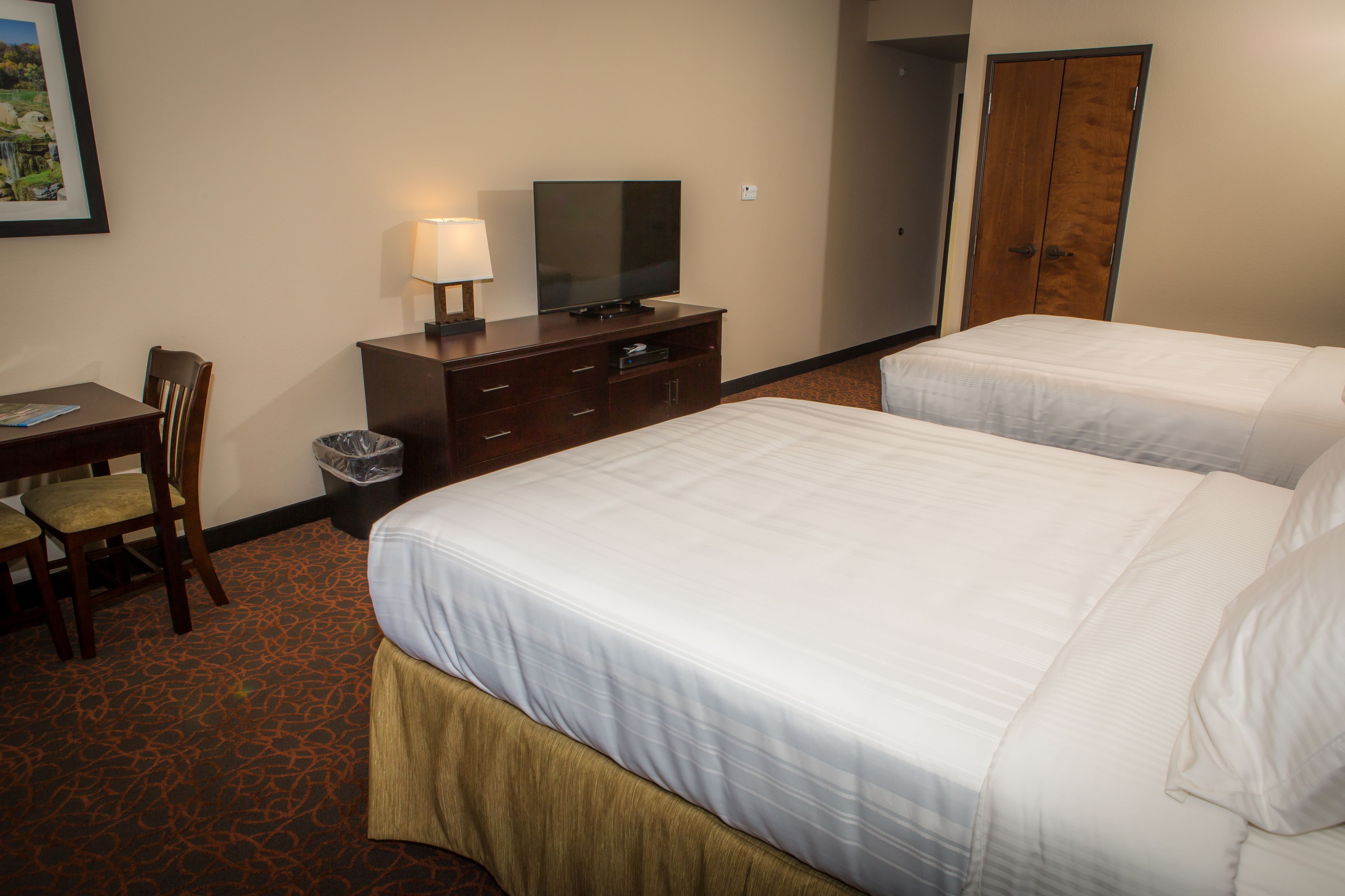 A hotel room with two beds, a desk with a chair, a television, and a trash can.