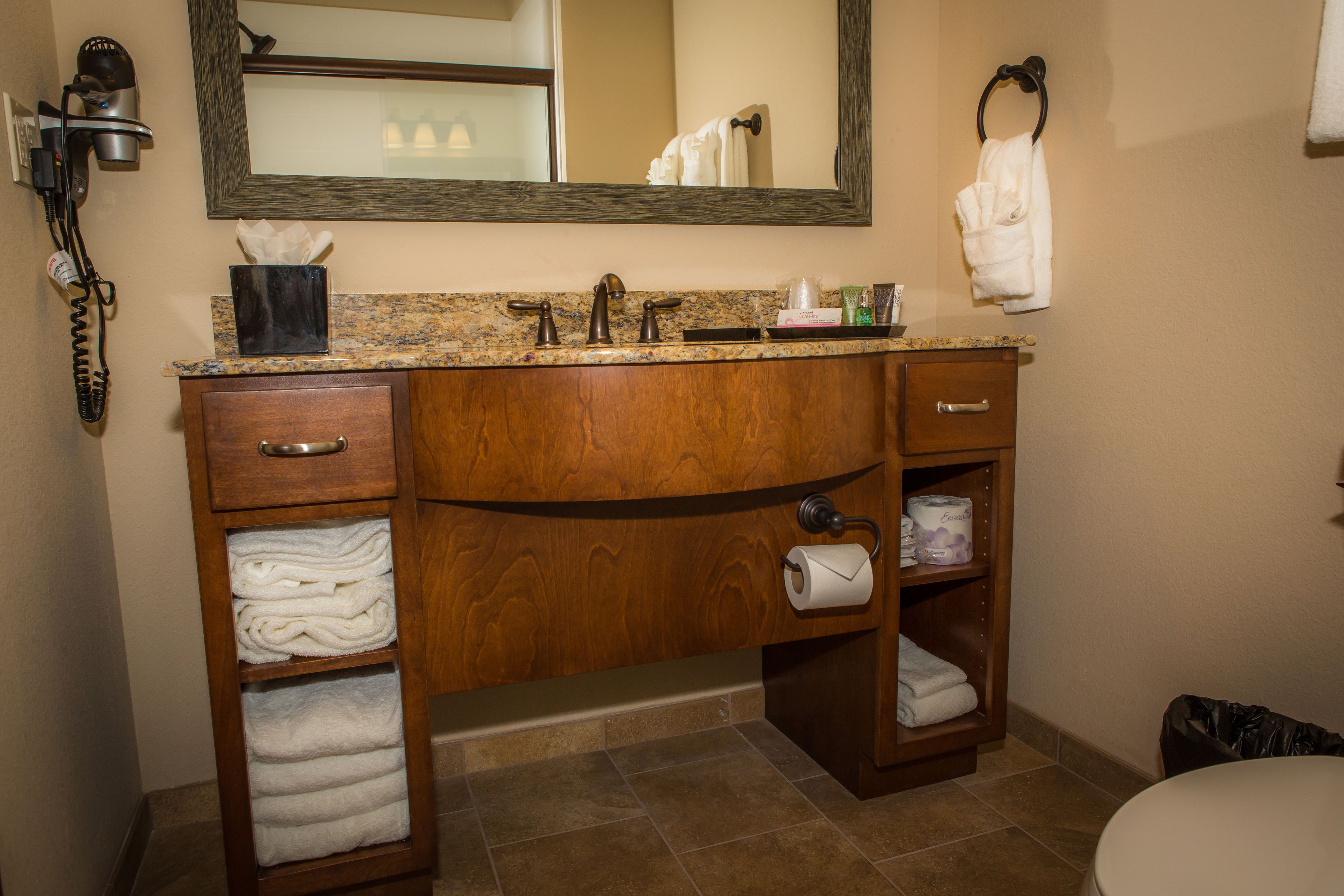 A bathroom with a wooden vanity, a sink, a mirror, and a toilet.