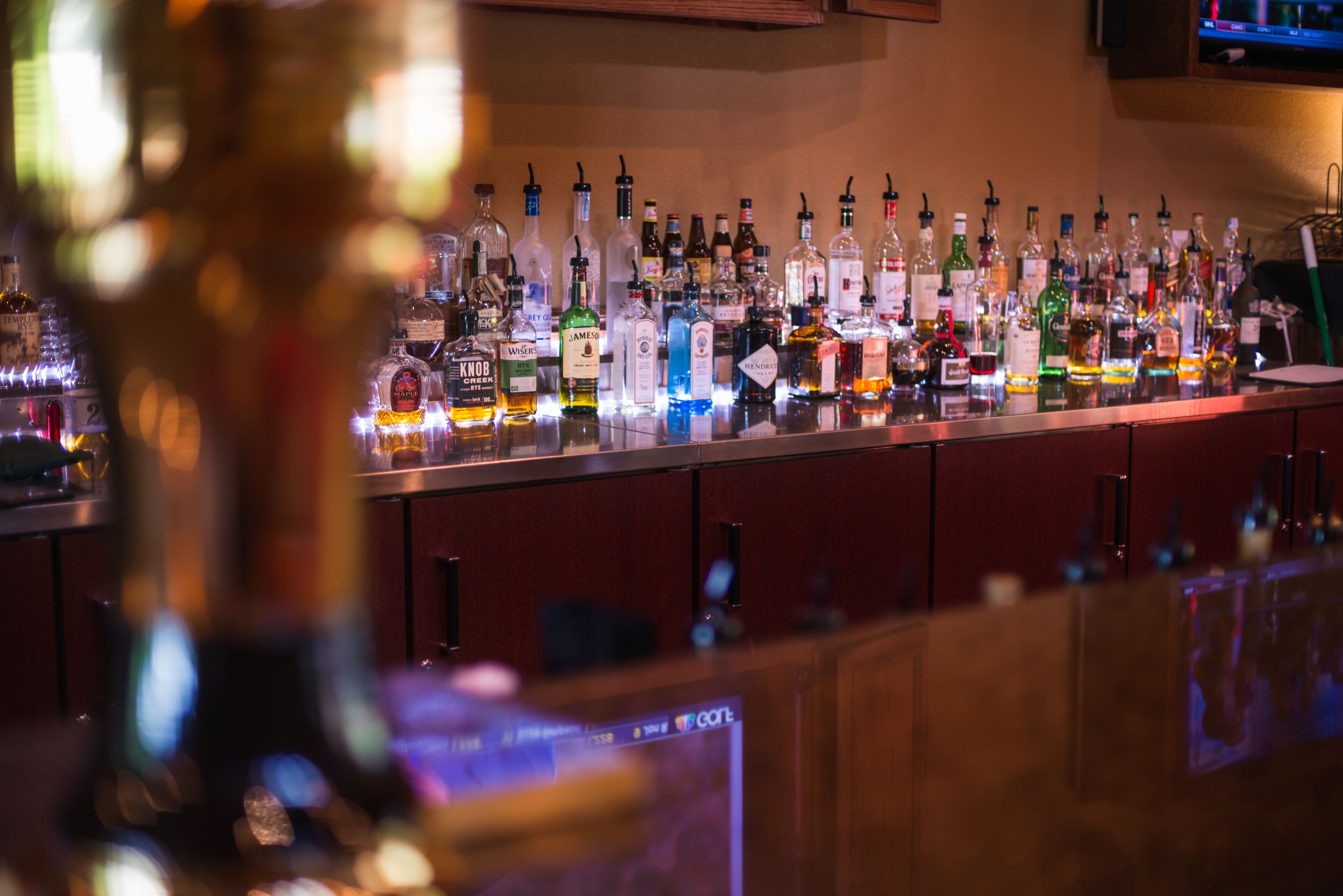 Un bar où l’on trouve une grande variété de bouteilles d’alcool, avec un écran de télévision en arrière-plan.