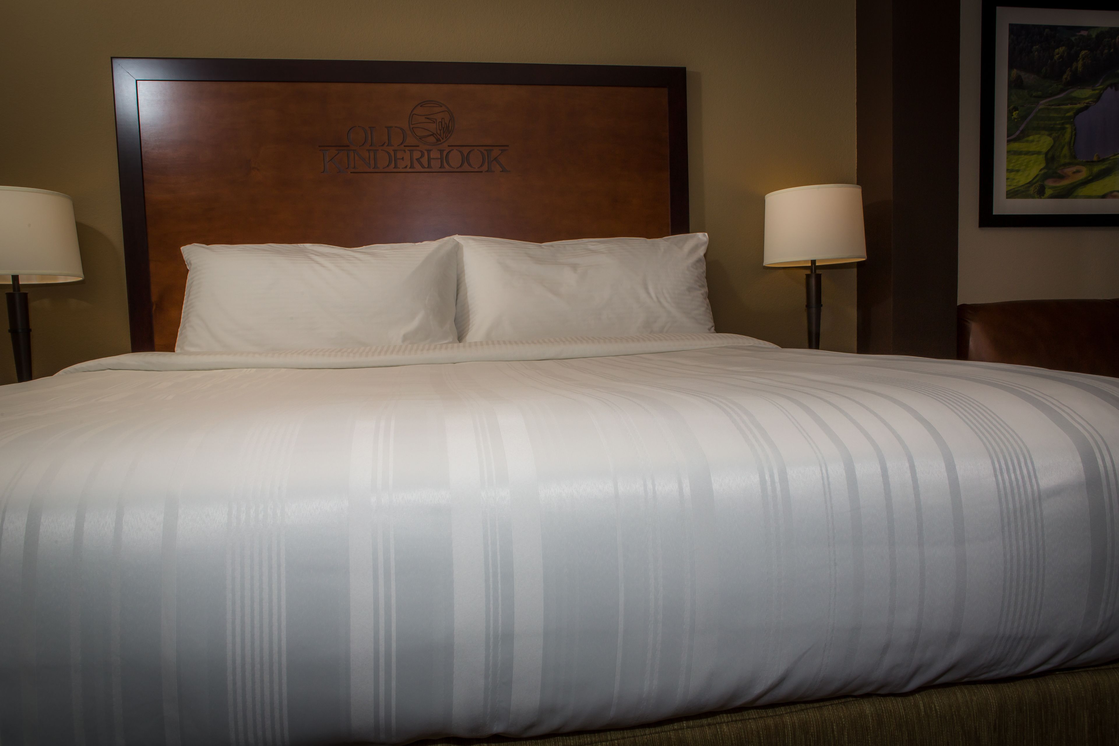 A neatly made bed with a headboard that reads "Old Dominion Hotel." There are two bedside lamps on either side of the bed.