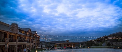 A hotel with a large outdoor pool, a covered area with string lights, and a view of the surrounding landscape.