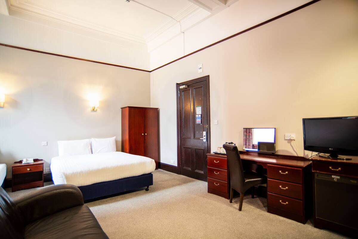 A hotel room with a bed, desk, chair, television, and wardrobe.