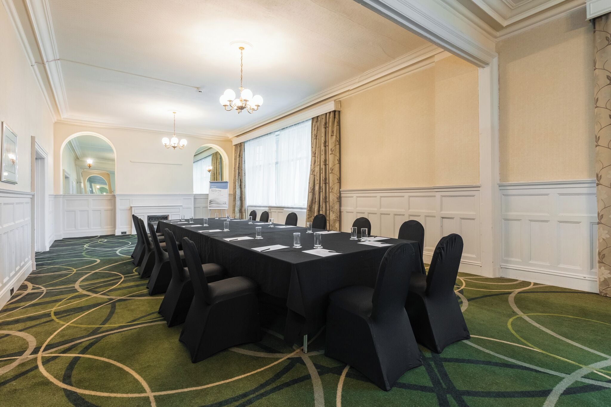 A conference room with a long table, chairs, a chandelier, and a carpeted floor.