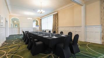 A conference room with a long table, chairs, a chandelier, and a carpeted floor.