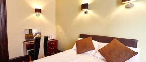A hotel room with a bed, a desk with a chair, and two wall-mounted lamps.