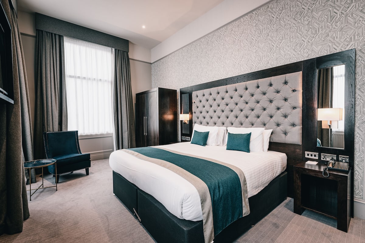 A hotel room with a large bed, a chair, a nightstand, and a mirror.