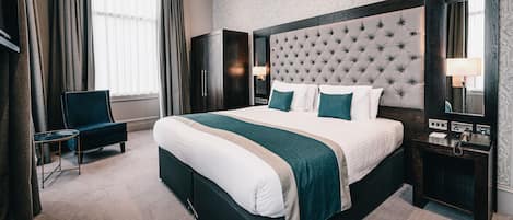 Ein Hotelzimmer mit einem großen Bett, einem Sessel, einem Nachttisch und einem Spiegel.