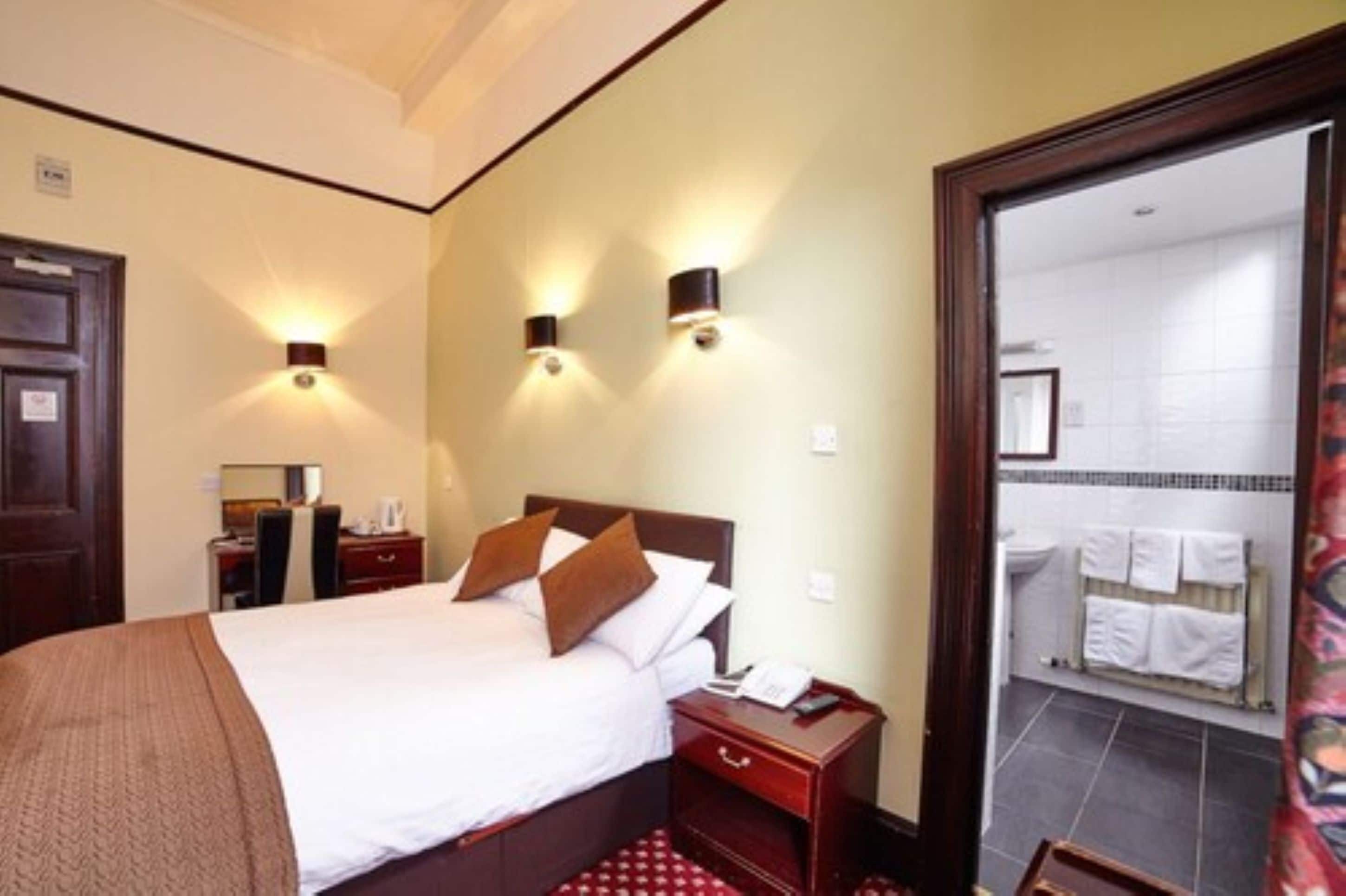 A hotel room with a bed, bedside tables, a telephone, and a bathroom visible through an open door.