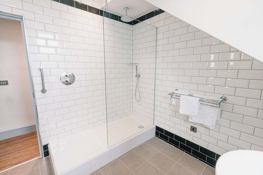 Un baño moderno con azulejos blancos tipo metro, ducha con cerramiento de vidrio y un perchero para toallas.
