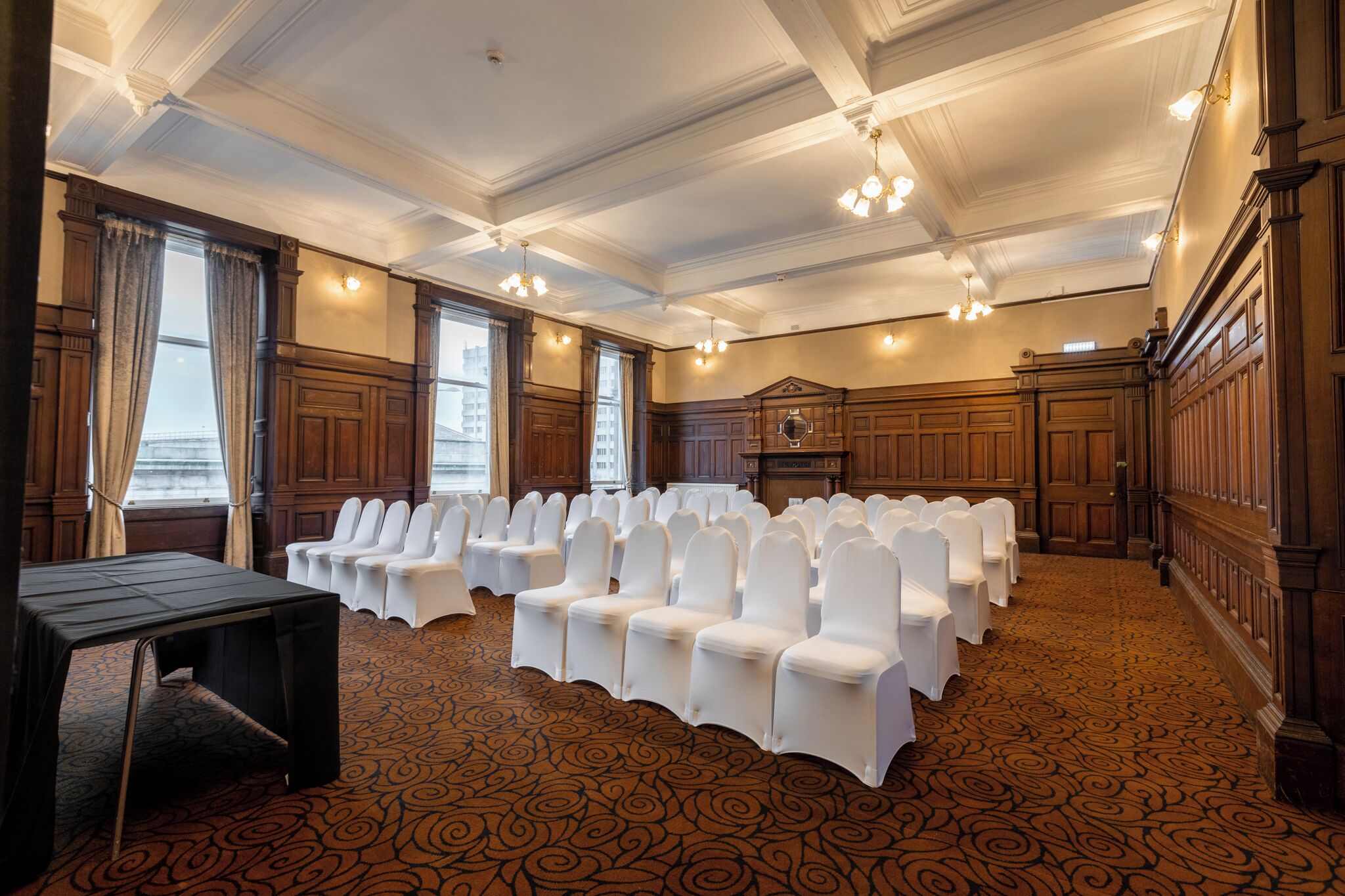 A conference room with rows of white chairs, wooden paneling, and a patterned carpet.
