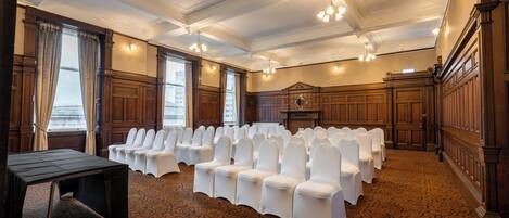 A conference room with rows of white chairs, wooden paneling, and a patterned carpet.