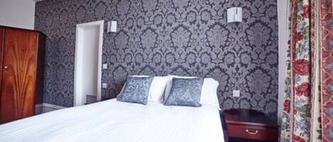 A bedroom with a bed, a wardrobe, a nightstand, and a patterned wallpaper.