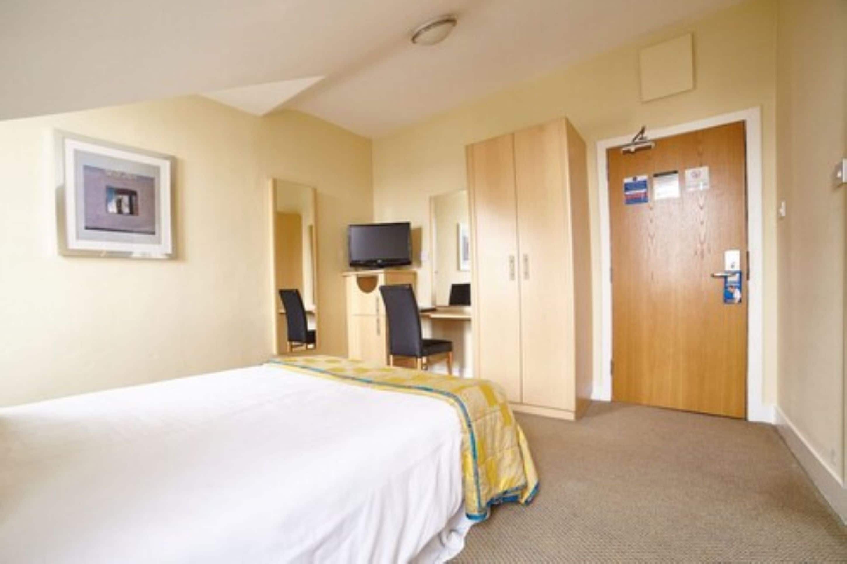 Une chambre d’hôtel comprenant un lit, un bureau avec une chaise, une télévision et une armoire.