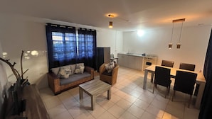 A living room with a sofa, armchair, coffee table, and dining area with chairs and a table. - Dive Hut - Boutique Apartments (Kralendijk)