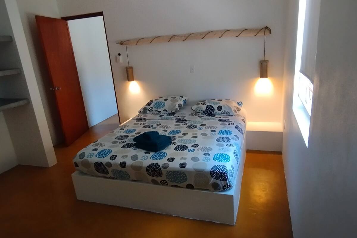 A bedroom with a bed, a wooden headboard, and two wall-mounted lights.