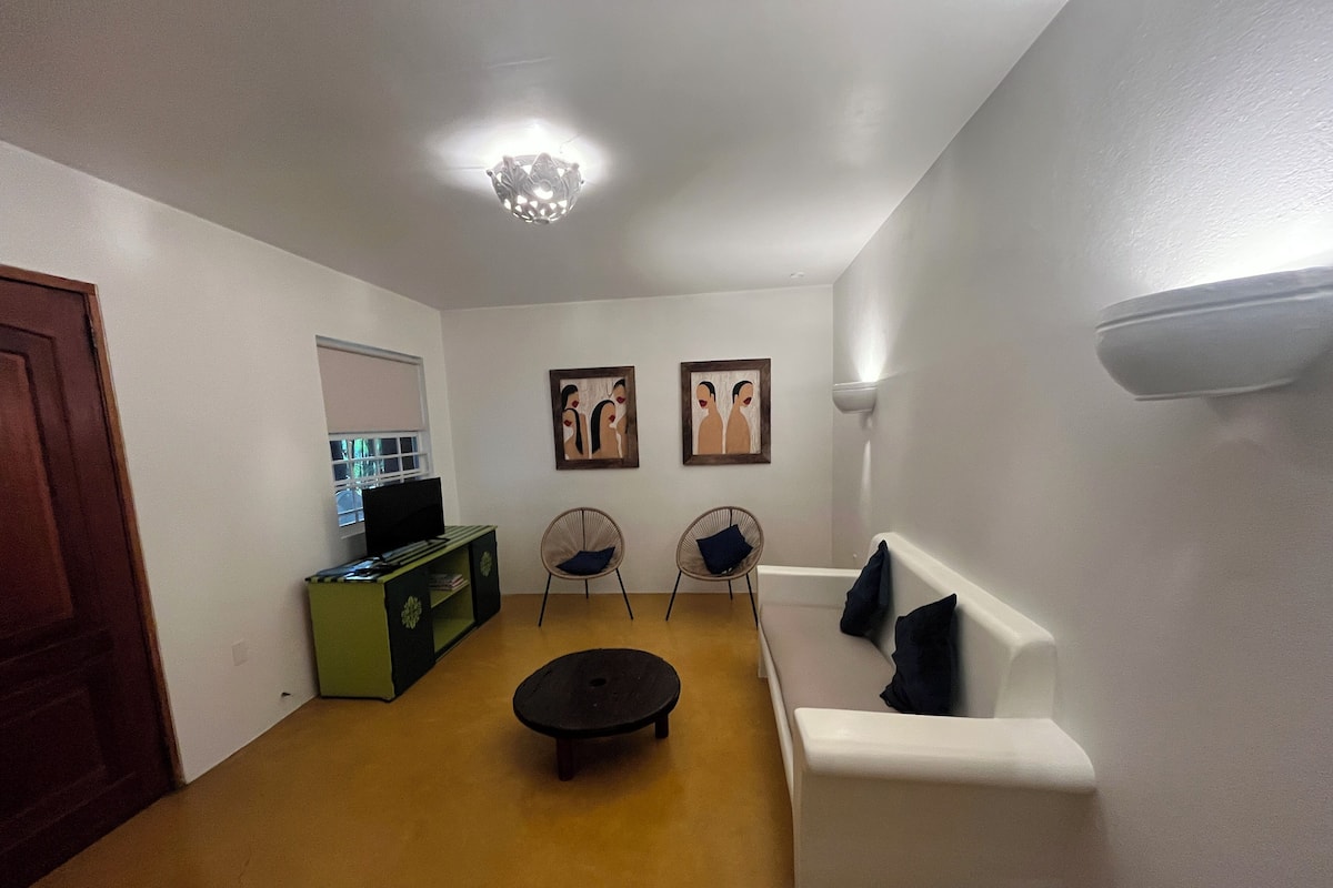 A living room with a white sofa, two chairs, a coffee table, and a TV on a green cabinet.